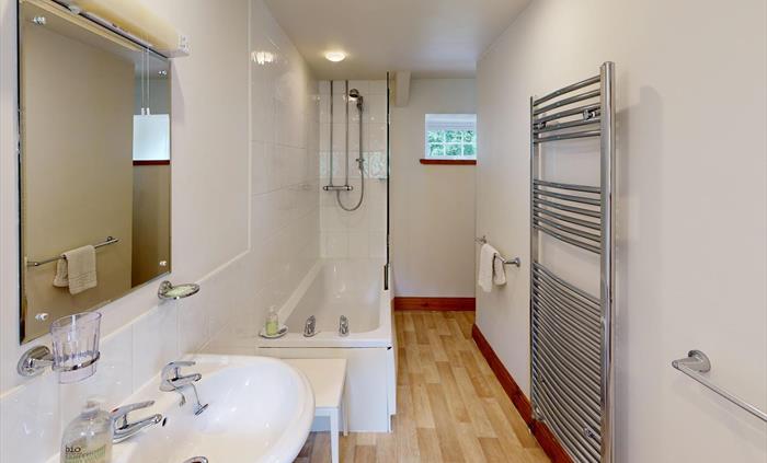 Clean, modern bathroom with bath, overhead shower, large mirror, and heated towel rail.